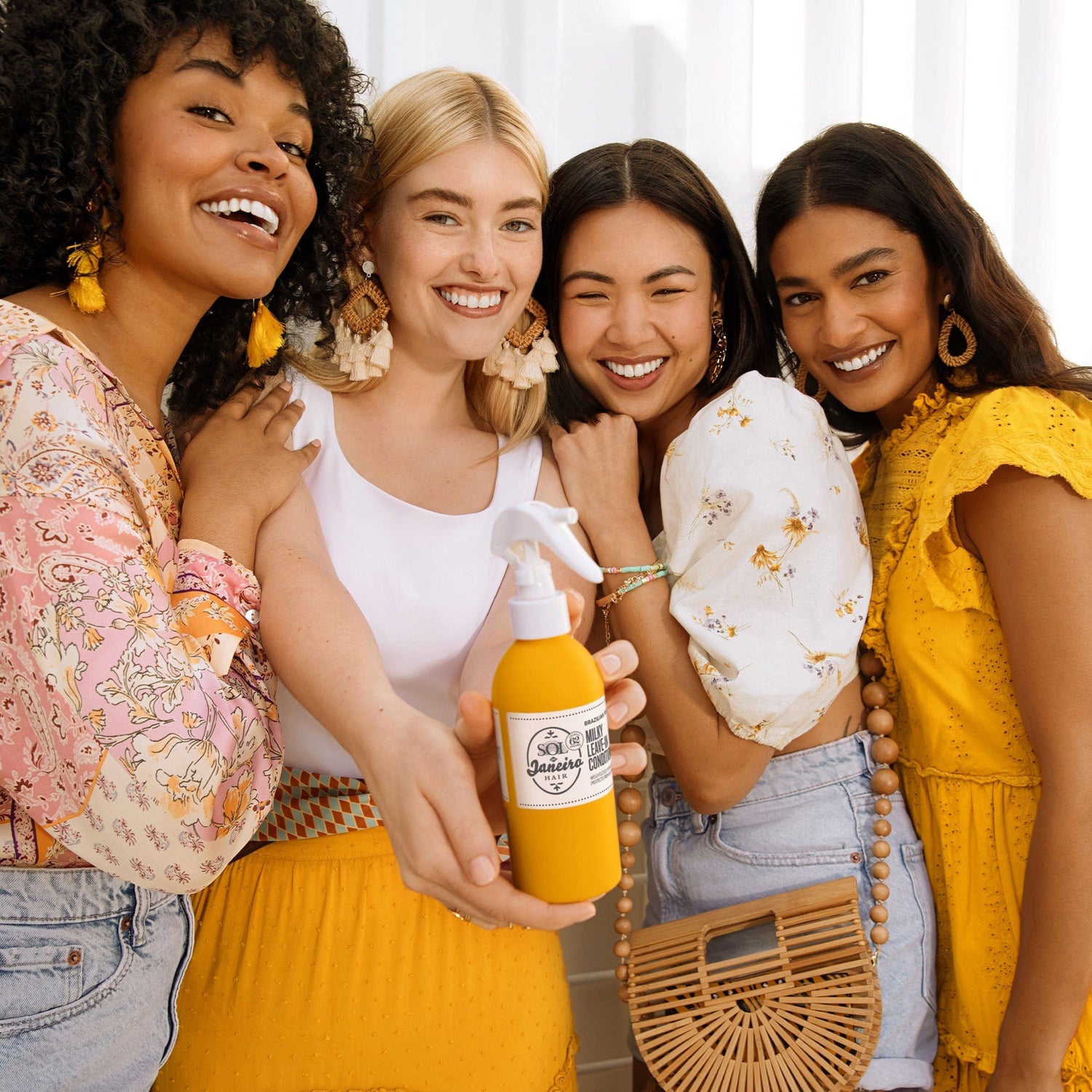 four women standing close together and one is holding Brazilian Joia Milky Leave in conditioner | Sol de Janeiro